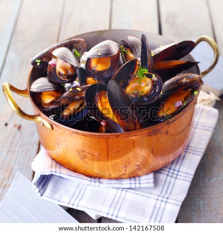 Copper pot of gourmet mussels served on a napkin garnished with fresh herbs for a tasty seafood meal