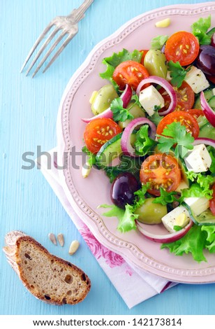 Overhead view of a serving of feta cheese salad with olives and cherry tomatoes on a embossed white plate with a slice of rye bread