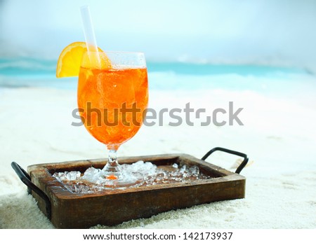 Tropical orange and daquiri cocktail standing on a wooden tray with crushed ice on a sunny beach on a summer vacation