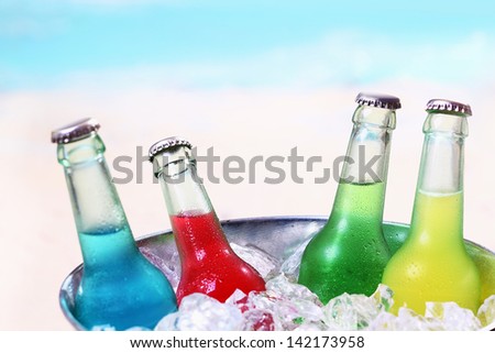 Colourful chilled soda drinks in unlabeled glass bottles standing in a metal container of crushed ice cubes for a summer party