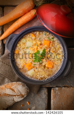 Top view of a warm and delicious freshly made pot of soup with raw carrots, chickpeas and a loaf of rustic bread