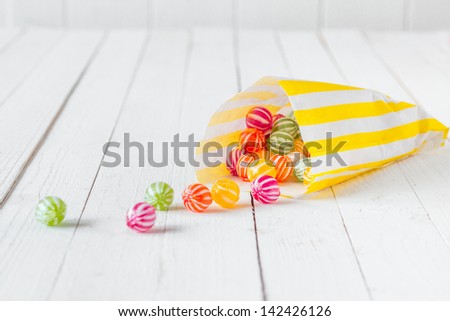 Yellow Striped Candy Bag Spilling Its Candies Over A White Wooden Table