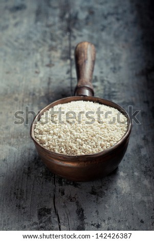 High-angle view of an old copper ladle filled with raw sesame over an old grungy grey wood table