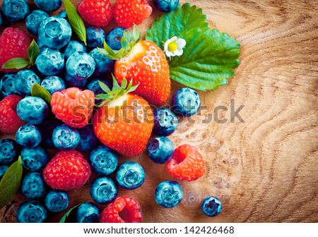 Overhead view of mixed ripe autumn berries including strawberries, raspberries and blueberries on a decorative woodgrain surface