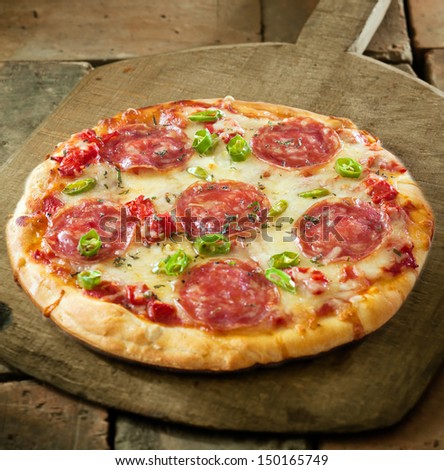 High Angle View Of A Whole Uncut Spicy Pepperoni Pizza Topped With Melted Cheese And Salami Slices On A Wooden Board