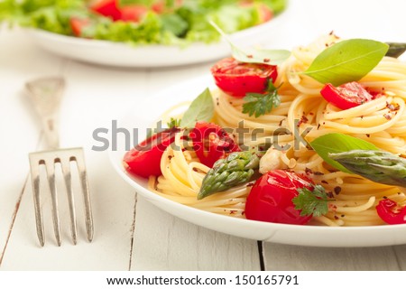 Vegetarian spaghetti pasta with fresh green asparagus spears, tomato and herbs served with a leafy green salad