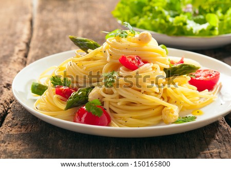 Low angle view of a plate of Italian spaghetti with fresh green asparagus spears and tomato served with a leafy green salad