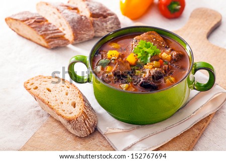 Tasty Winter Stew In A Green Metal Pot With Meat And Assorted Vegetables In A Rich Gravy Served With Fresh Crusty Bread On A Wooden Chopping Board