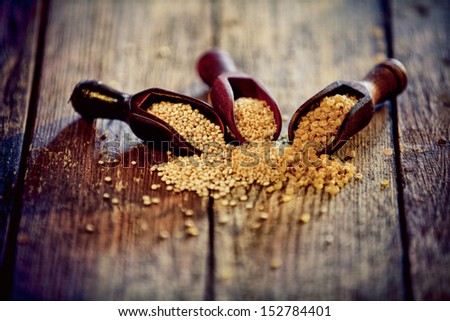 Variety of cereal grains spilling out of wooden scoops onto an old wood countertop including bulgur and couscous