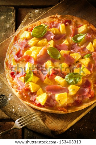 High angle view of an exotic ham and pineapple pizza on a crisp golden crust served on a wooden board