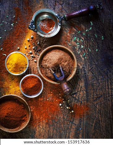 Overhead View Of Colourful Dried Ground Spices In Bowls Spilling Onto An Old Aged Scored Wooden Surface In A Country Kitchen With A Vintage Sieve Or Strainer