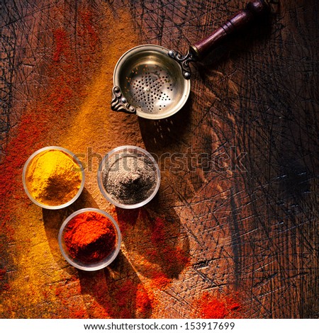 Overhead view of three bowls of spice in a country kitchen on an old scored wooden surface with scattered powder and an old retro strainer or sieve