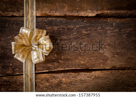 Festive gold ribbon and bow border to the left of the frame over a grunge dark textured rustic wood background with copyspace for your Christmas, anniversary or birthday wishes or invitation