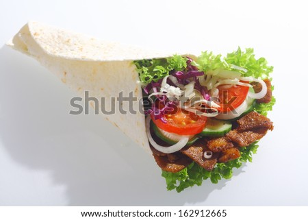 Doner or corn taco wrap filled with grilled meat and fresh salad filling including lettuce, tomato, onion and cucumber on a white background