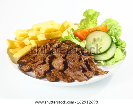 Plate of grilled beef nuggets, fried potato chips or French fries and fresh leafy green salad with cucumber on a white background