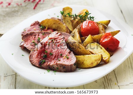 Delicious succulent rare beef steak sliced and served with roast potato wedges and tomato garnished with chopped parsley