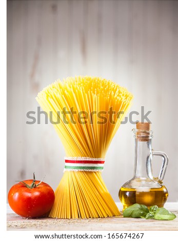 Uncooked dried Italian spaghetti tied with a ribbon in the colours of the national flag - red, white and green, standing upright on a kitchen counter with fresh tomato and basil and a jar of olive oil