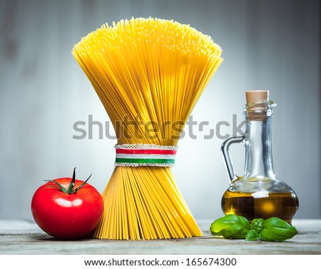 Bundle Of Uncooked Dried Italian Spaghetti Tied With A Ribbon In The Colours Of The National Flag - Red, White And Green - With A Decanter Of Olive Oil, Basil And A Tomato