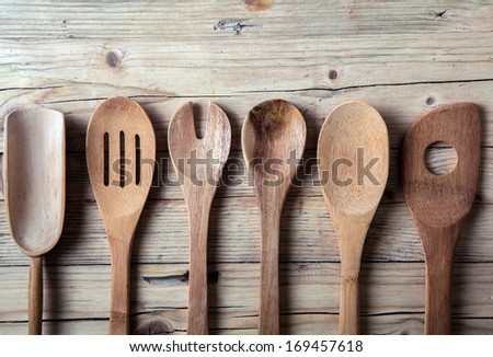Row of assorted old wooden kitchen utensils lying on a grungy cracked wooden surface in a country kitchen
