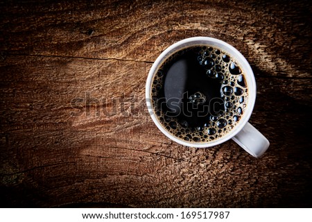 Close up overhead view of a cup of strong frothy espresso coffee on a rough textured wooden surface with dark vignetting and a highlight around the mug, with copyspace
