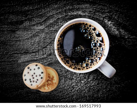 Overhead view of a cup of freshly brewed hot espresso coffee served on a weathered grunge rustic wooden table wiith two iced biscuits