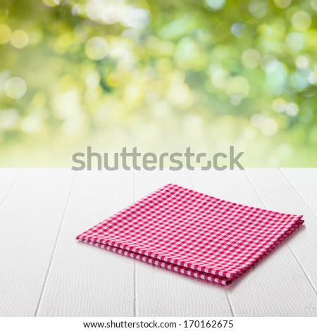 Neatly folded fresh red and white checked cloth conceptual of a country or rustic ambiance on a garden table in a sunny summer garden with focus to the napkin