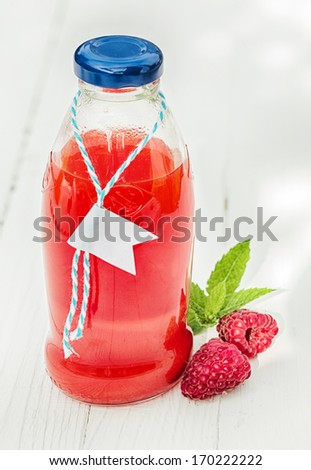 Homemade fresh raspberry juice in a glass bottle made from freshly squeezed fruit together with two fresh berries on a rustic white wooden background