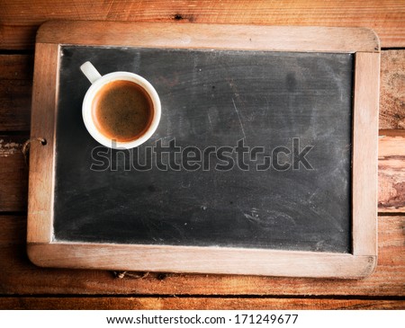 Overhead View Of A Cup Of Coffee On An Old School Slate With A Wooden Frame And Blank Copyspace On The Cleaned Chalkboard Lying On A Rustic Wooden Table