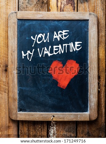 Vintage style chalkboard over old wood background, with the message You are my Valentine written in white chalk next to a red chalk heart