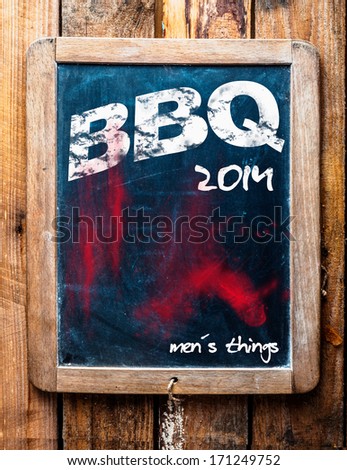 BBQ advertised on an old vintage school slate in a grunge wooden frame on a rustic table with an addendum at the bottom saying - Mans stuff