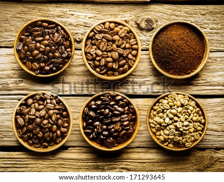 Five Varieties Of Coffee Beans And Ground Powder Is Separate Dishes Showing The Different Strengths And Colour Of The Beans From Raw Through Medium To Full Roast On A Weathered Driftwood Background