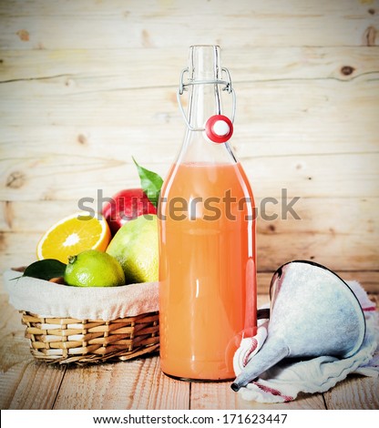 Fresh tropical fruit juice in a glass bottle alongside a basket of assorted fruit used as ingredients and a small metal funnel to facilitate pouring