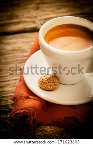 Morning coffee break with a cup of aromatic rich frothy espresso and a macaroon served in a rustic kitchen on a weathered old wooden surface, closeup high angle view
