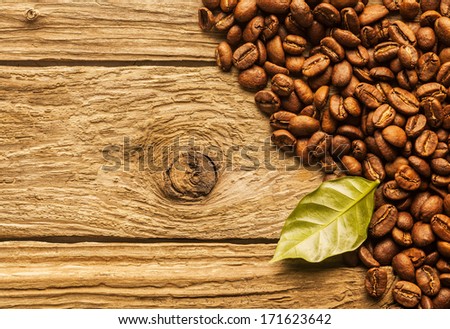 Pile of fresh roasted coffee beans arranged as a corner border on textured rustic wood boards with a green coffee leaf and copyspace