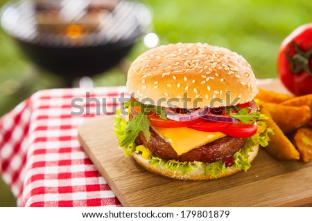 Tasty cheeseburger with melted cheddar cheese dripping over ground beef burger garnished with fresh salad ingredients and served on a wooden table on an outdoor picnic table