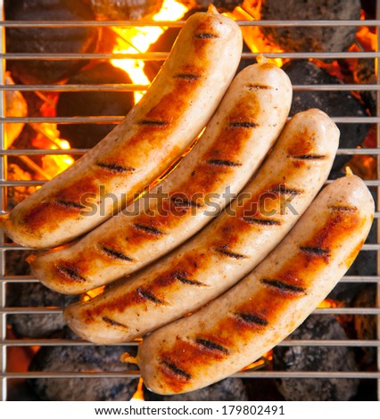 Delicious sausages called bratwurst, on a metal grid grilling over hot coals on a BBQ for a picnic lunch on a summer vacation