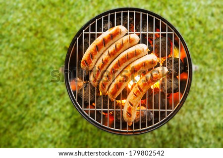 View from above on a green grass background of a row of pork and beef bratwurst grilling over a barbecue fire on a hot day during the summer vacation