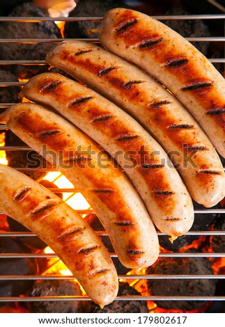 Row of tasty browned seared pork and beef sausages cooking over the hot coals on a barbecue fire, close up overhead view