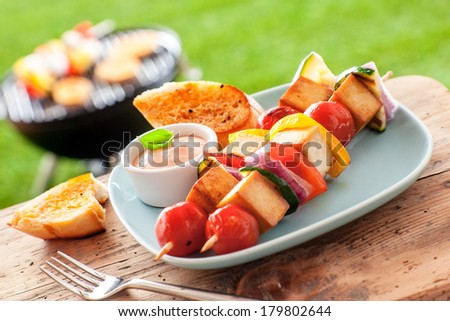 Outdoors Summer barbecue on a table with a tofu kebab and a grill in the background