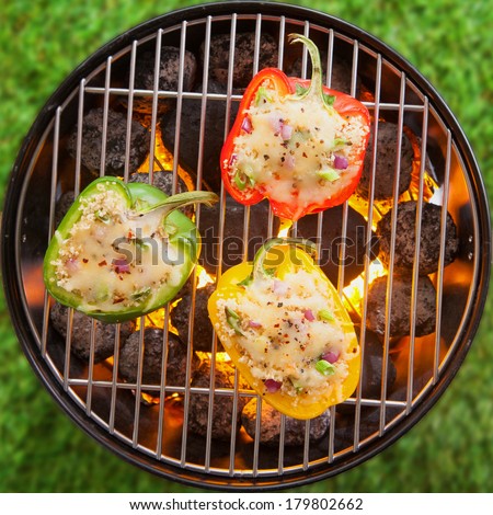 Overhead view on green grass of grilling stuffed savory bell peppers topped with melted cheese over the fire on an outdoor summer BBQ or picnic