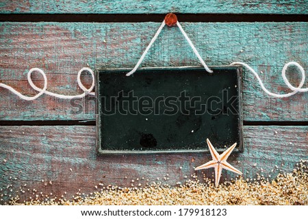 Blank slate for your seafood menu or advertisement hanging on grungy weathered blue wooden boards with sea sand and a starfish in a pretty marine background