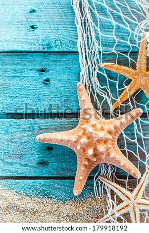 Colorful oceanic background with a marine still life of spiny starfish hanging on diamond mesh fish net on weathered rustic turquoise painted boards with copyspace and beach sand