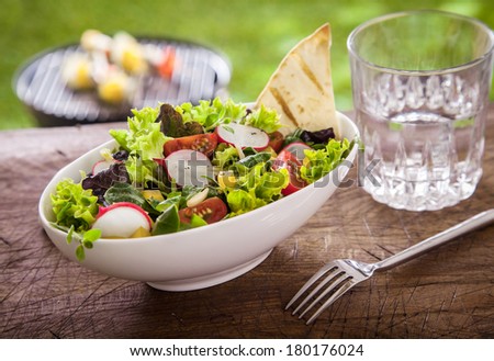 Healthy summer salad with lettuce, bell pepper, tomato and radish served with a glass of fresh water on a rustic wooden garden table
