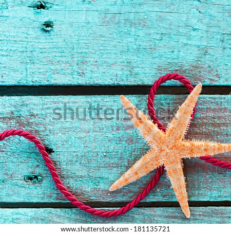 Colourful nautical themed background of an orange starfish with looped red rope on turquoise wooden boards with copyspace for your text in square format