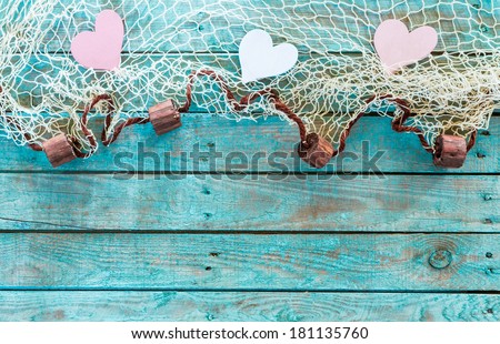 Pretty pink and white hearts in a fishing net border with corks symbolising love and romance on turquoise blue wooden boards for your Valentines,anniversary or wedding greeting, horizontal format