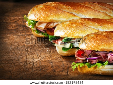 Three tasty baguettes with savory fillings lined up on a rustic wooden countertop with roast beef and rocket, figs and cheese, and chicken and salad fillings