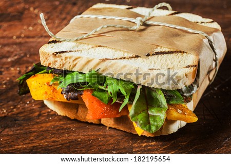 Takeaway grilled toasted sandwich with pepper,cheese,rocket, spinach and leafy green herbs tied with a brown paper wrapper and string