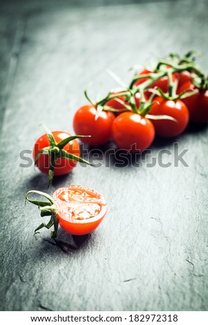 Grape tomatoes on the vine with a single halved tomato in the foreground on a textured surface with highlight and copyspace and shallow dof