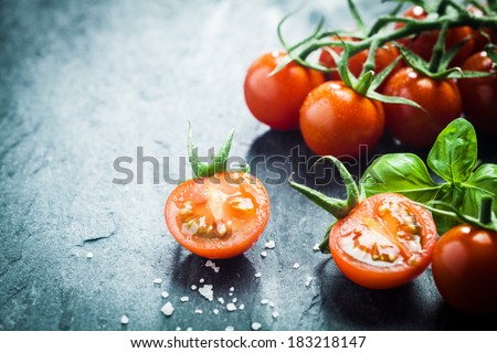 Fresh grape tomatoes with basil and coarse salt for use as cooking ingredients with a halved tomato in the foreground with copyspace