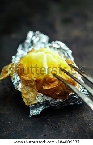 Half eaten delicious baked jacket potato in aluminium foil for a healthy vegetarian diet or accompaniment to a picnic or barbecue